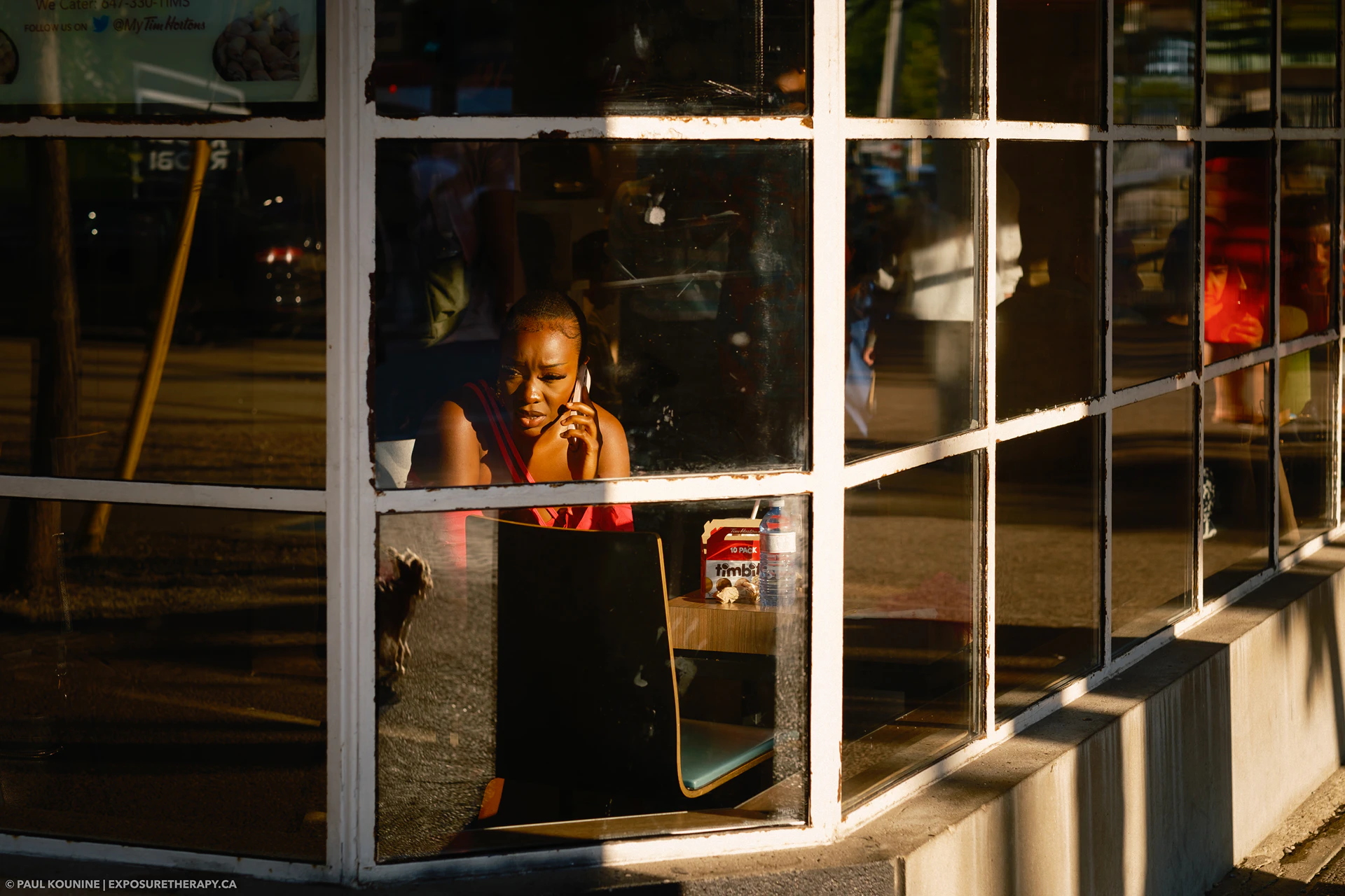 Woman on phone in Tim Horton's during sunset along Queens Quay in Toronto.